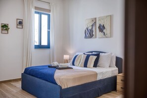 A bedroom with a bed, a window with curtains, a bedside table, and wall art.