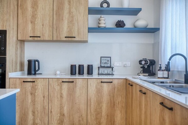 A modern kitchen with wooden cabinets, a coffee station, and a built-in oven.