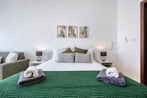 A hotel room with a bed, two bedside tables, a green blanket, and two towels.