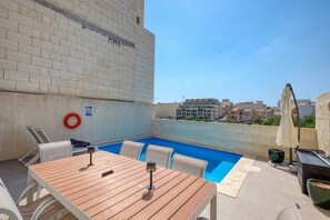 An outdoor swimming pool area with a wooden table and chairs, a life ring, and a grill.