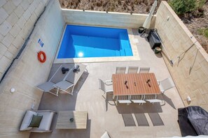 Une piscine sur le toit, avec des chaises longues, une table et des chaises, ainsi qu’un barbecue.
