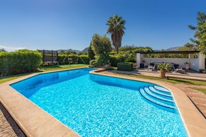 A rectangular swimming pool with clear blue water, surrounded by a well-maintained garden with various plants and a swing set. - Pollensa Country Villa for 6 (Pollença)