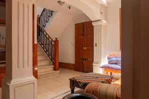 A hallway with a staircase, a wooden door, and a bed with colorful bedding.