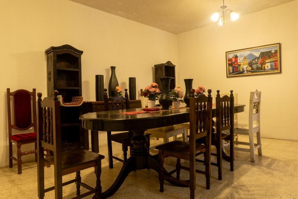 A dining room with a round table, wooden chairs, a chandelier, and a painting on the wall.