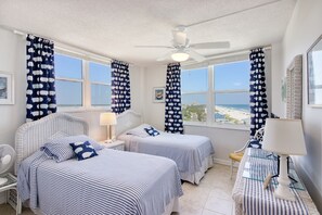 Een kamer met twee bedden, een plafondventilator en uitzicht op het strand.