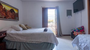 Un dormitorio con una cama, televisión, un cuadro y una ventana con cortinas.