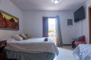 Ein Schlafzimmer mit Bett, Fernseher, einem Gemälde und einem Fenster mit Vorhängen.