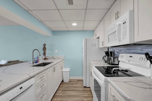 A modern kitchen with white cabinetry, a stainless steel sink, a microwave, a stove, and a trash can. - Ocean View Oasis | Walk to Carolina Beach! (Carolina Beach)