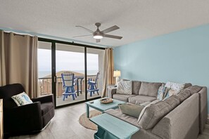 A room with a sofa, a chair, a small table, and a view of the ocean through a sliding door. - Ocean View Oasis | Walk to Carolina Beach! (Carolina Beach)