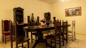 Un comedor con una mesa redonda, sillas de madera, una araña y un cuadro en la pared.