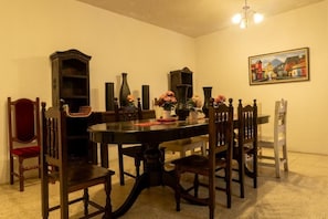 Een eetkamer met een ronde tafel, houten stoelen, een kroonluchter en een schilderij aan de muur.