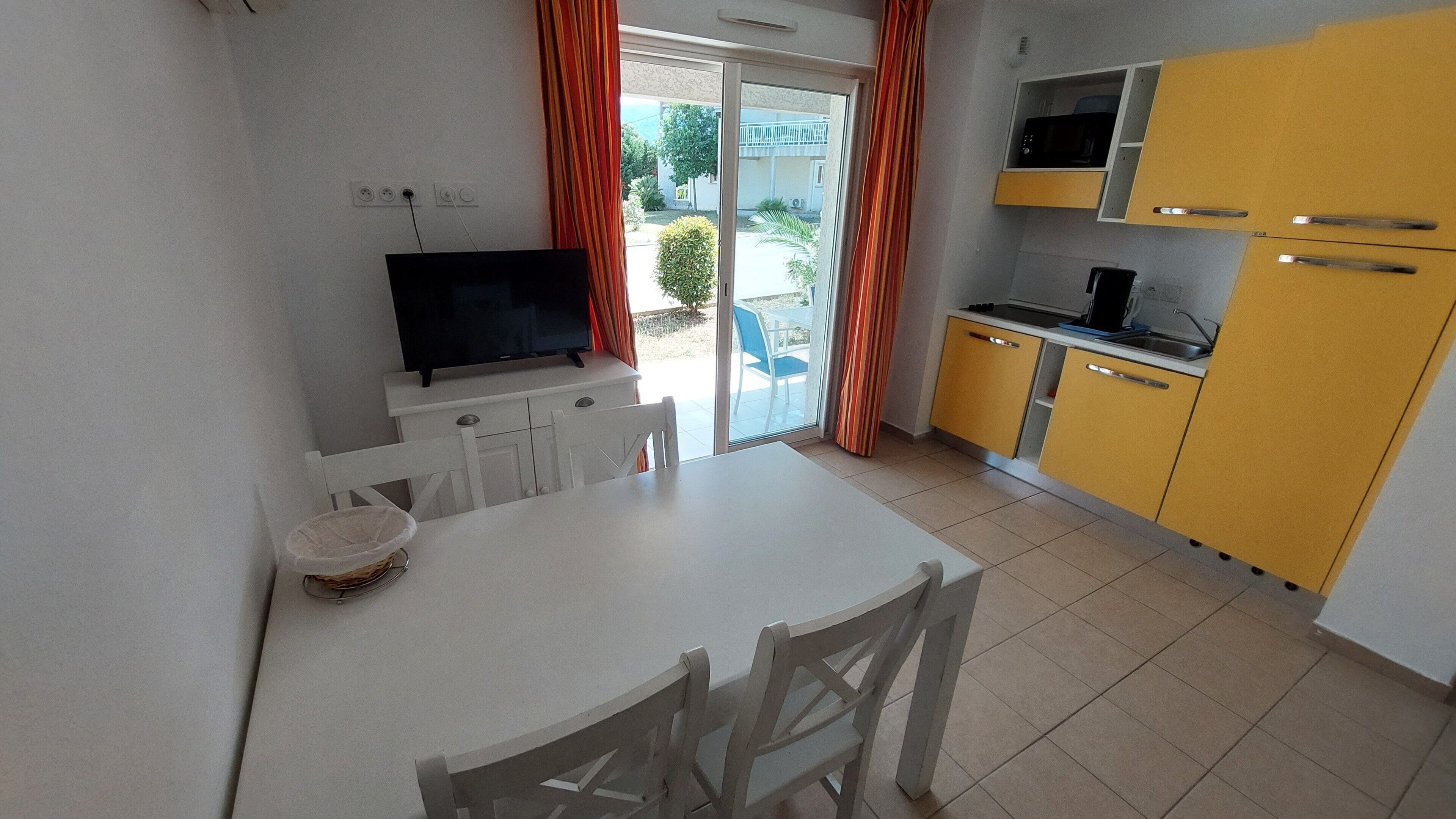 Una cucina compatta con angolo ristoro, televisione e una porta scorrevole in vetro che dà su uno spazio esterno.