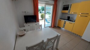 A compact kitchen with a dining area, a television, and a sliding glass door leading to an outdoor space.