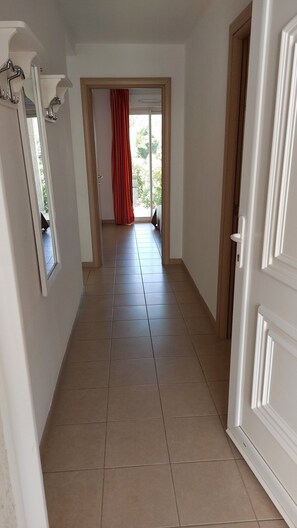A hallway with a tiled floor, a door on the right, and a window with a view of greenery outside.