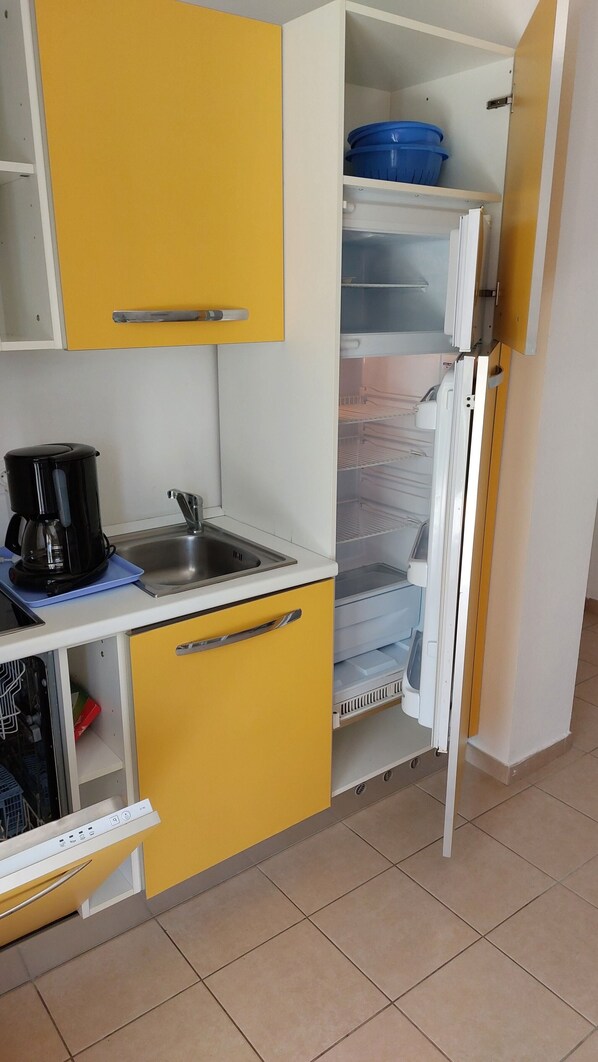 A compact kitchen with a coffee maker, a sink, and a refrigerator with shelves.
