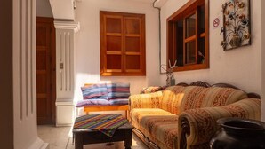 Habitació amb un sofà, una panxa i una finestra amb persianes de fusta.