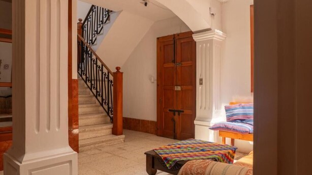 Un passadís amb una escala, una porta de fusta i un llit amb roba de llit colorida.
