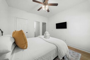 A bedroom with a bed, a ceiling fan, a white door, and a flat-screen TV on the wall. - Gata suite close to GSU and paulson stadium (Statesboro)