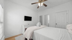 Ein Schlafzimmer mit einem Bett, einem Flachbildfernseher an der Wand, einem Deckenventilator und einer weißen Tür.
