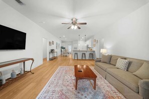 A spacious living room with a wooden coffee table, a beige sofa, and a large flat-screen TV mounted on the wall. - Gata suite close to GSU and paulson stadium (Statesboro)