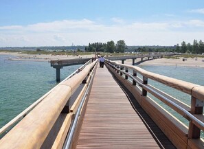 A wooden boardwalk leading to a beach with a clear view of the water and distant buildings. - Holiday Apartment With 2 Bedrooms (Heiligenhafen)