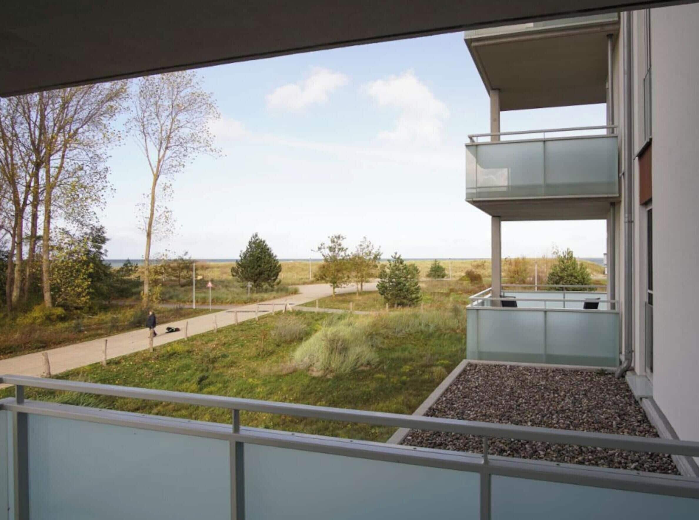 A modern building with a balcony overlooking a grassy area with trees and a clear sky.