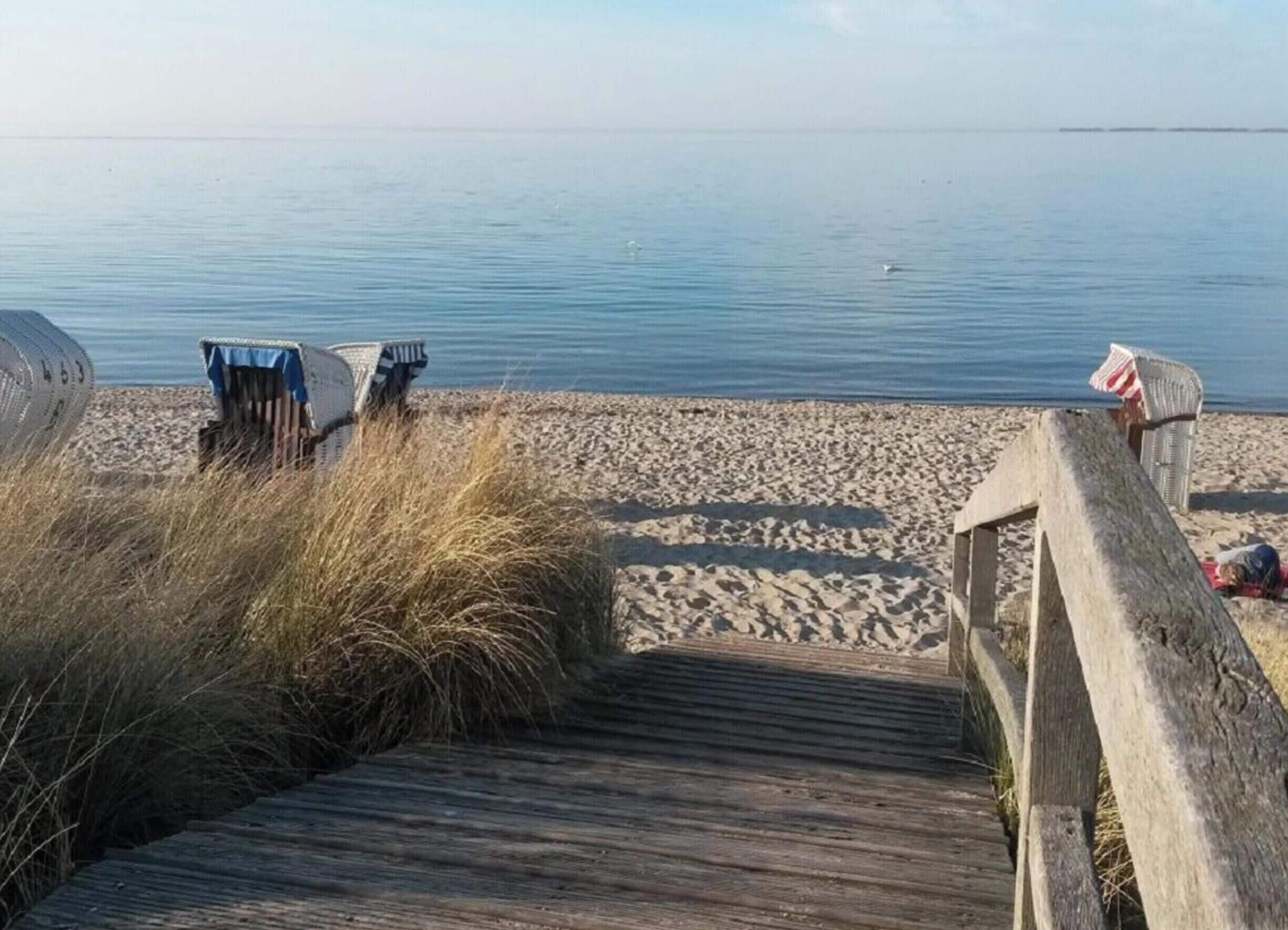 A wooden boardwalk leading to a sandy beach with calm water in the background.