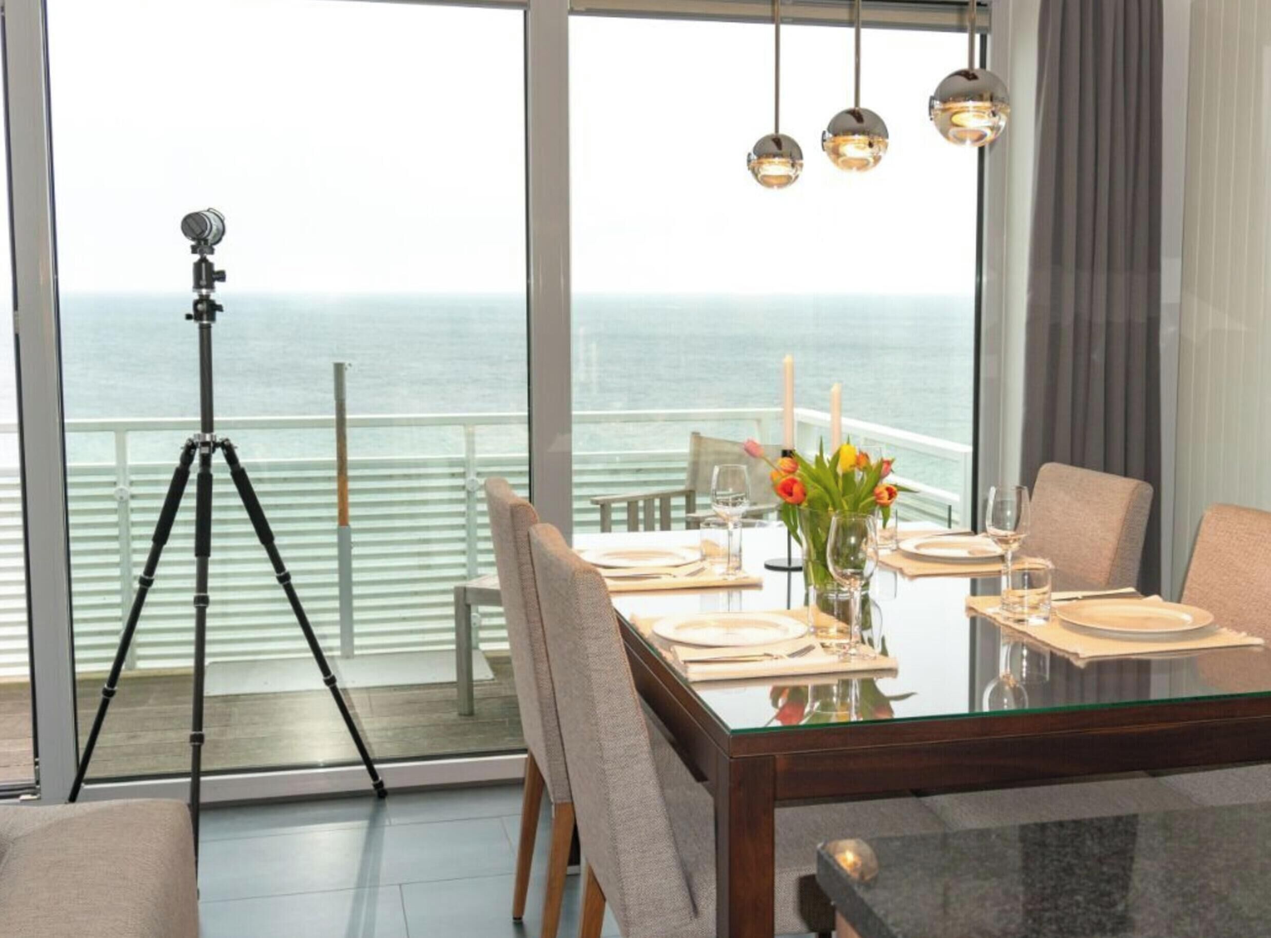 A dining area with a glass table, chairs, and a view of the sea.