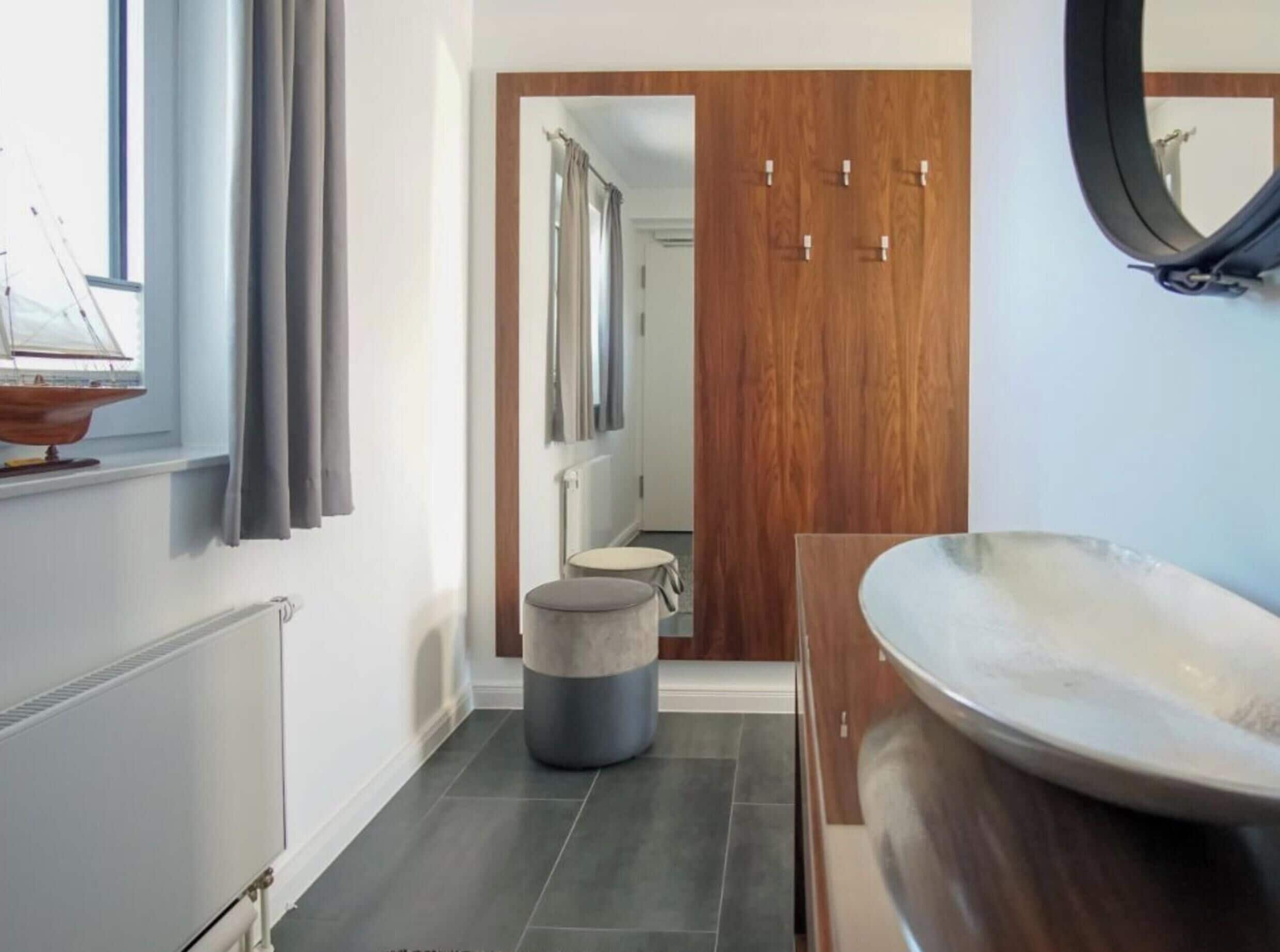 Ein modernes Badezimmer mit Holztür, rundem Spiegel und einer großen Badewanne.