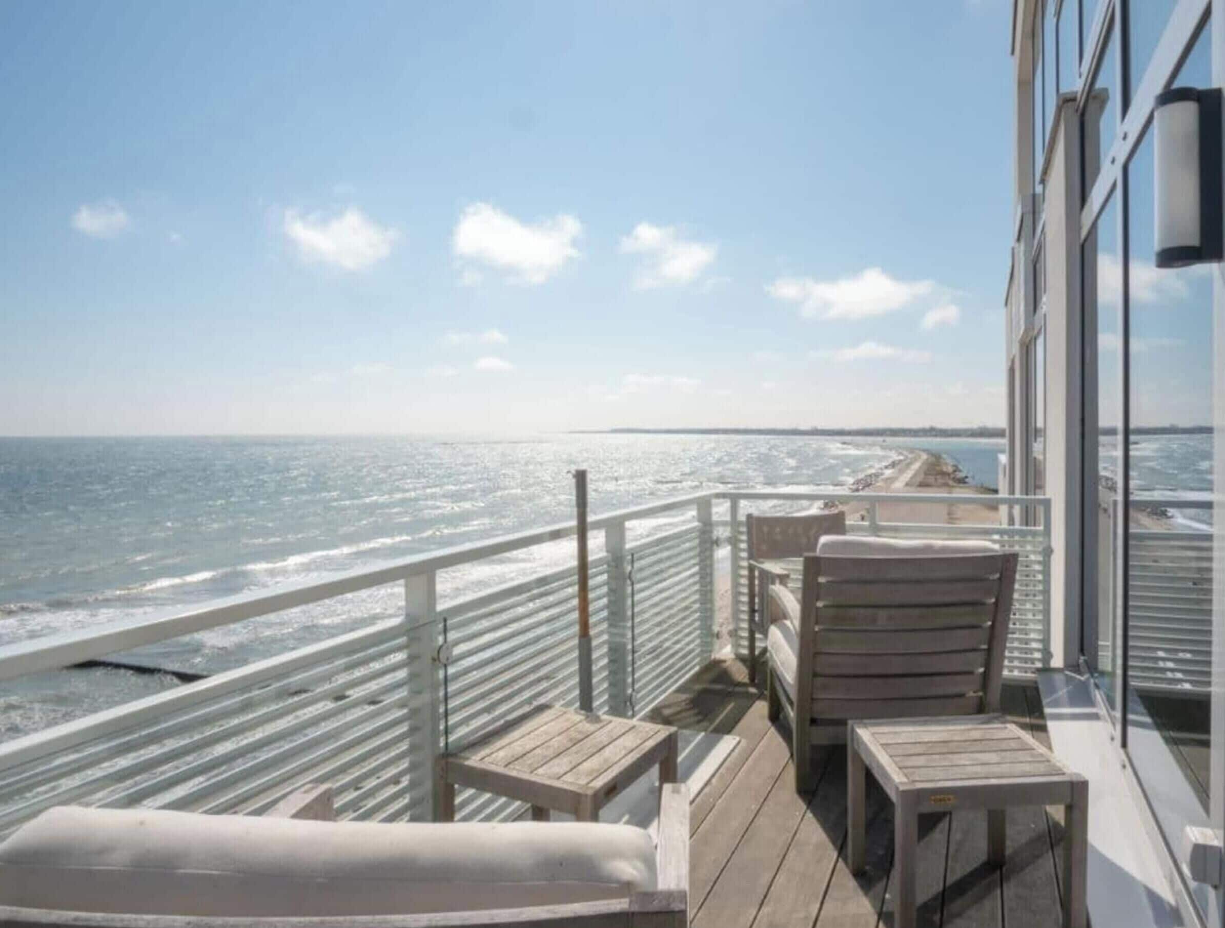 Un balcon doté de mobilier en bois, offrant une vue sur une plage et l’océan.
