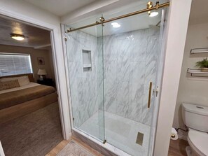 Een moderne badkamer met een douchecabine van glas, marmeren wanden en een zichtbaar toilet.