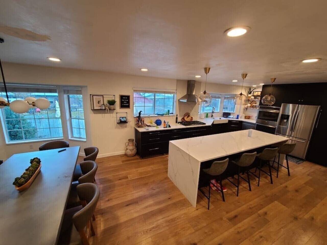A modern kitchen with a central island, wooden flooring, and pendant lighting.