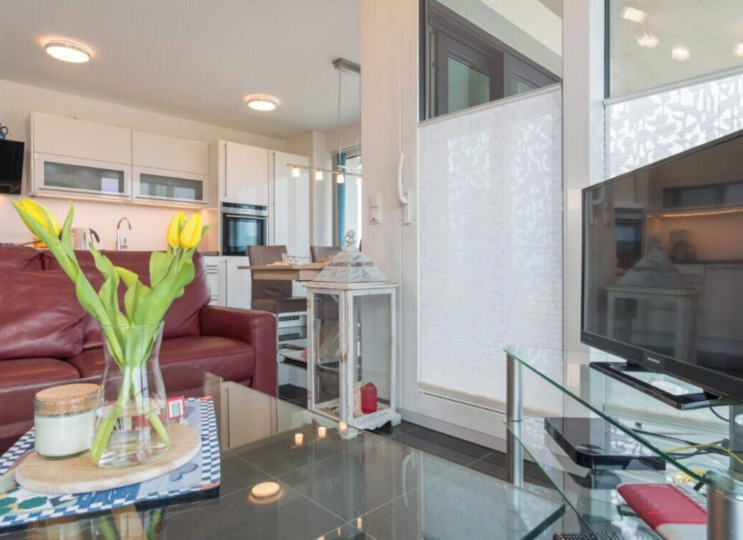 Ein modernes Wohnzimmer mit einem Glastisch, einem roten Ledersofa und einer Vase mit gelben Blumen.