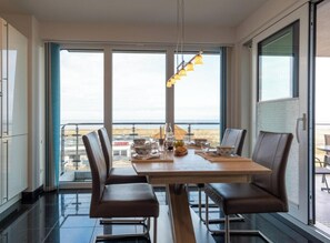 A dining area with a table set for two, two chairs, a hanging light fixture, and a view of the sea through large windows. - Holiday Apartment With 2 Bedrooms (Heiligenhafen)