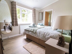 Ein Schlafzimmer mit einem Bett, einem Nachttisch, einem Spiegel, einem Fenster mit Vorhängen und einer Heizung.