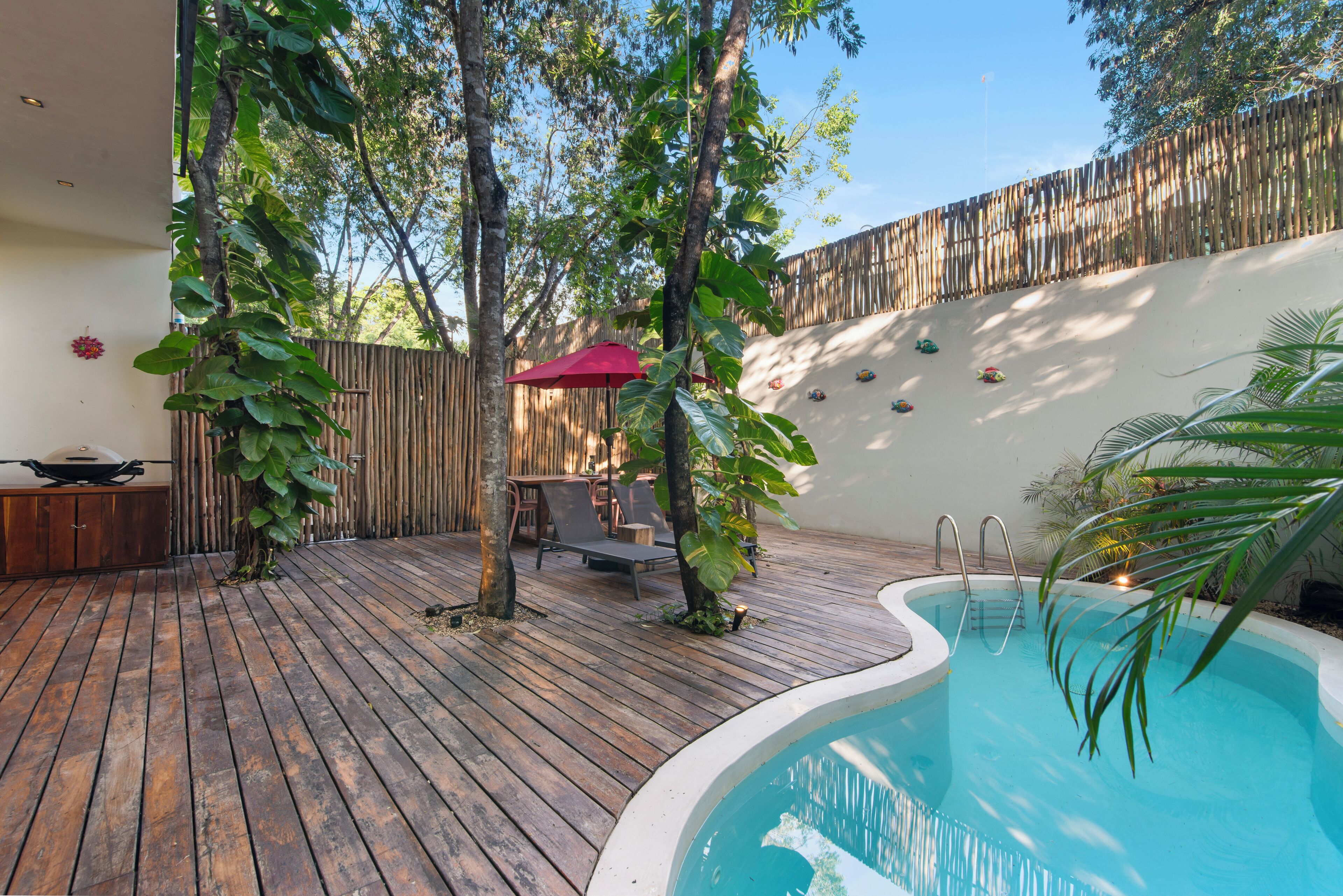 A wooden deck with a pool, surrounded by trees and a bamboo fence.