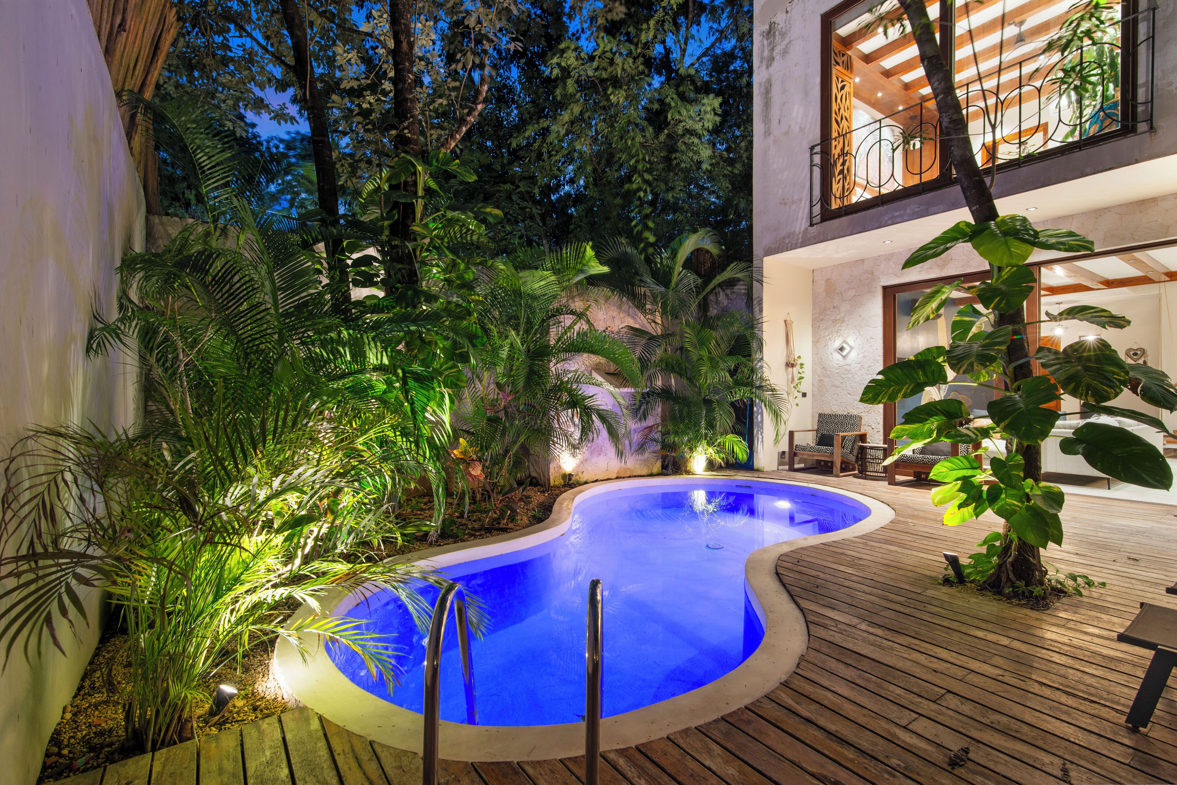 Ein Swimmingpool, umgeben von tropischer Vegetation und Holzterrasse.
