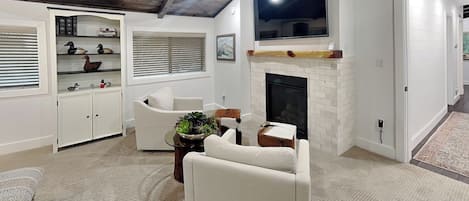Un soggiorno con camino, arredamento bianco, televisore a parete e libreria con oggetti decorativi.