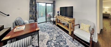 Una sala de estar con sofá, mesa de comedor, televisor y alfombra estampada.