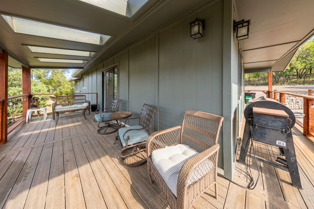 A covered deck with wicker furniture, a grill, and a view of the outdoors.