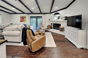 A modern living room with a sofa, a leather chair, a fireplace, a television, and a dining area with a table and chairs. - Amigos Nest (Alto)