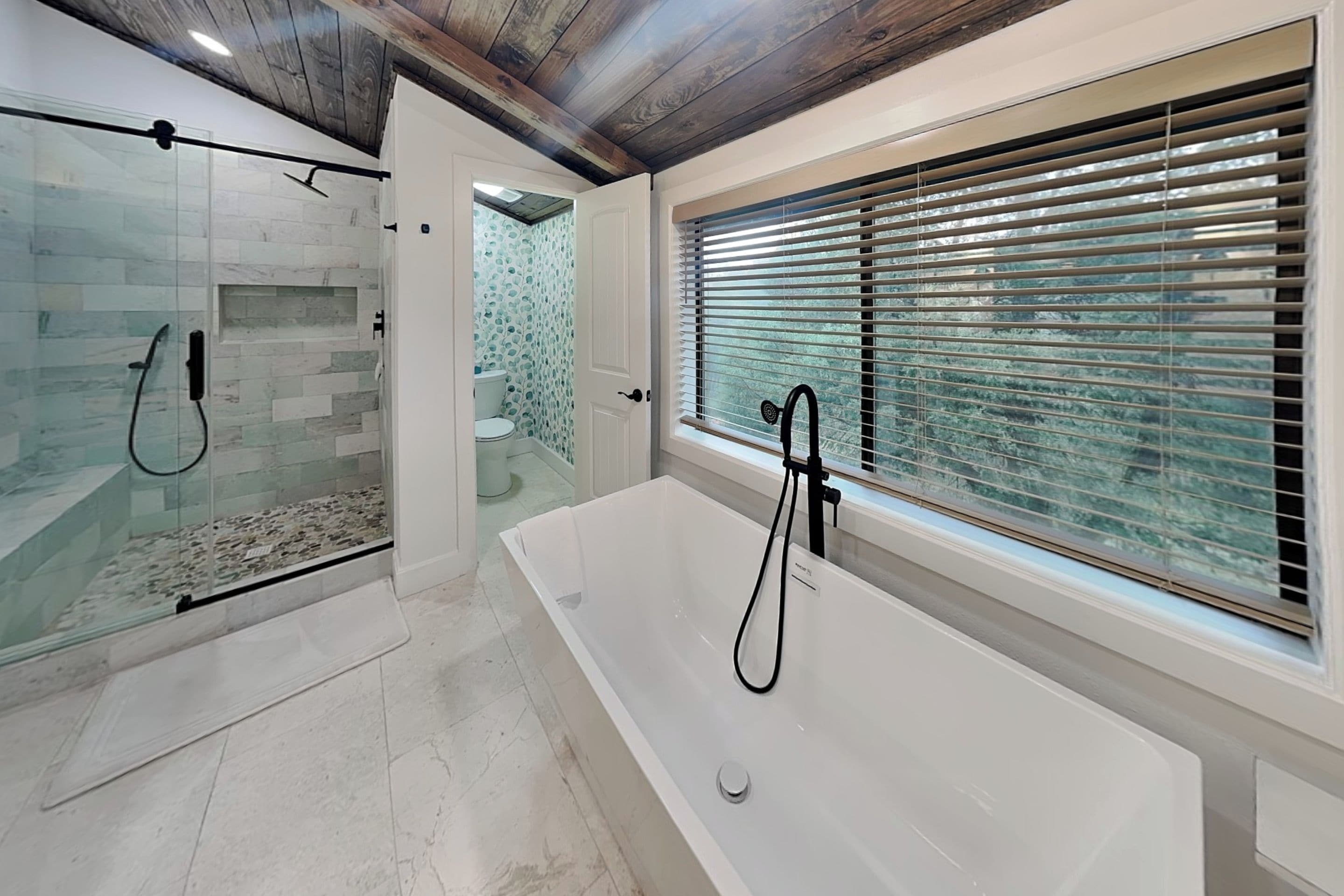 Ein modernes Badezimmer mit einer gläsernen Duschkabine, einer freistehenden Badewanne und einem Fenster mit Jalousien.