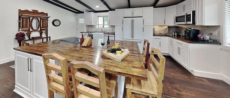 Une cuisine spacieuse avec des meubles blancs, un îlot central en bois doté de tabourets, et un four encastré.