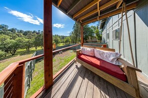 Eine Holzterrasse mit einer roten gepolsterten Bank mit Blick auf eine Rasenfläche.