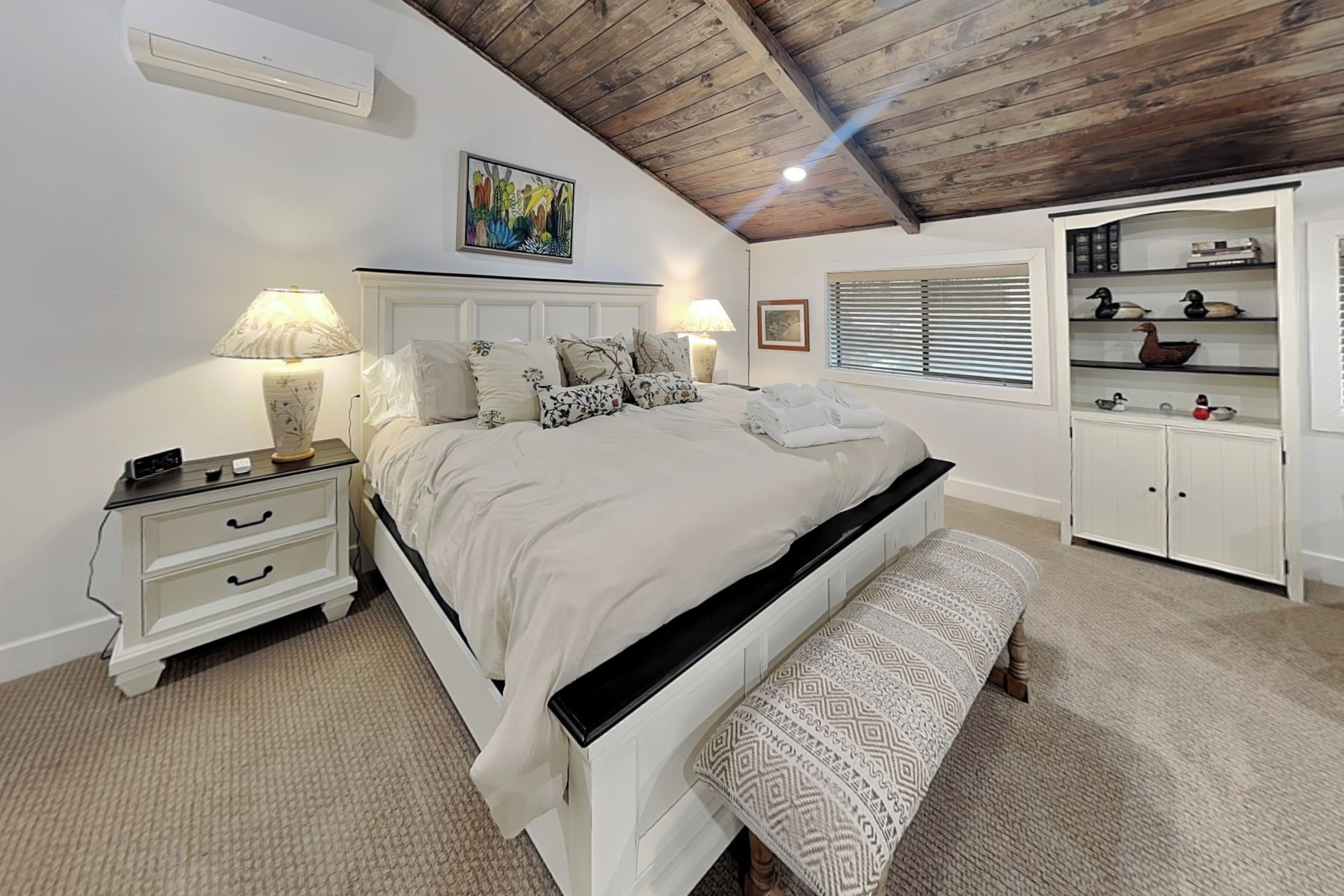 Een slaapkamer met een bed, nachtkastjes, een bankje, een kledingkast en een plafondventilator.
