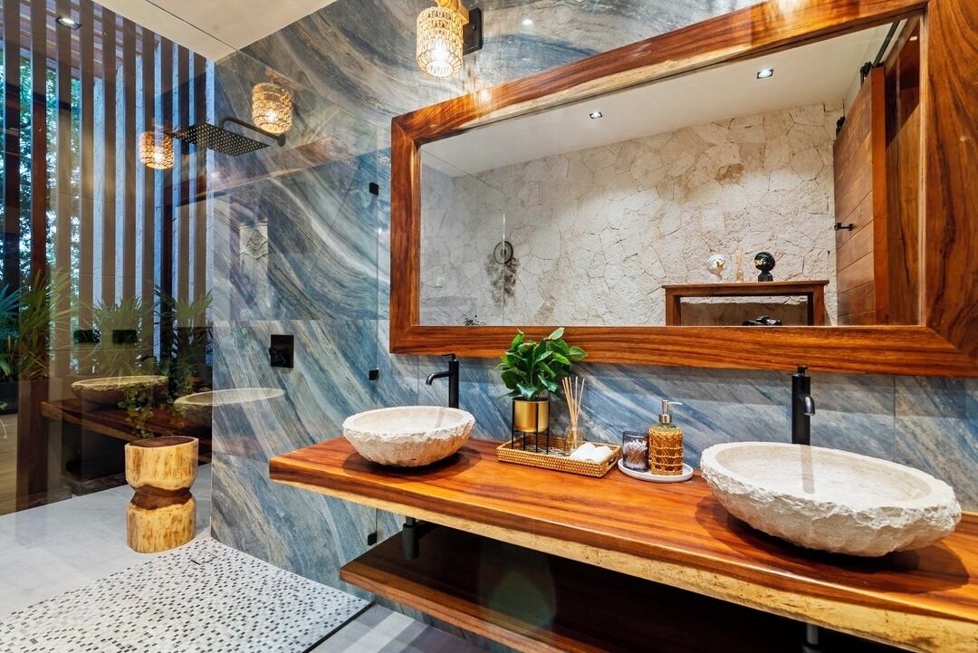 A modern bathroom with a wooden vanity, two stone sinks, a large mirror, and a decorative plant.