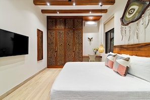 A bedroom with a large bed, a TV mounted on the wall, a wooden wardrobe, and a decorative headboard. - LUX 4BR/4.5 Bath Jungle Villa - Private Pool+Jacuzzi+Staff - BLUE DEER TULUM (Tulum)