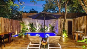 Eine Terrasse im Freien mit Holzdeck, zwei Holzstühlen, einem Tisch, einem großen Sonnenschirm und einem kleinen Pool mit umlaufenden Pflanzen.