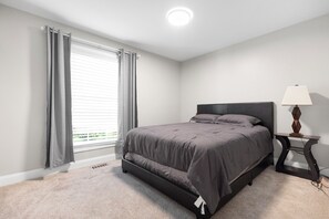 Een slaapkamer met een bed, een nachtkastje met een lamp en een raam met gordijnen.
