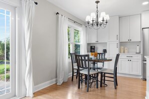 Cozinha moderna com armários brancos, uma mesa de jantar com cadeiras e um lustre.